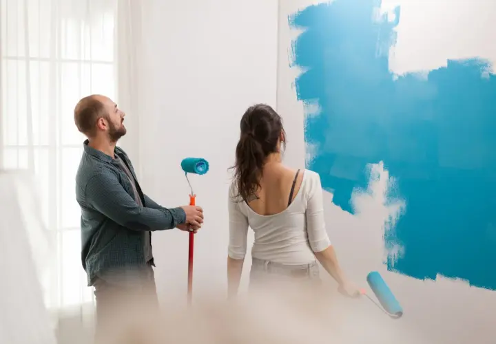 Pareja pintando una pared de azul. Él mira al techo, ella pinta. ¿Qué se pinta primero el techo o las paredes?