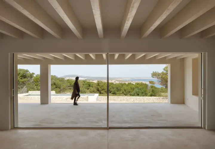 Persona camina por una terraza moderna con grandes ventanales que muestran varios tipos de ventanas correderas, vistas al mar y vegetación.