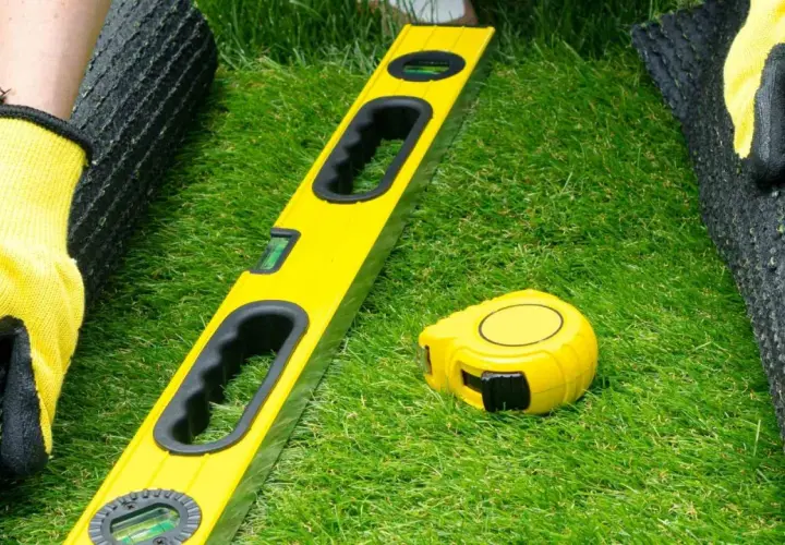 Manos enguantadas preparan el césped artificial. Nivel y cinta métrica listos para pegar.