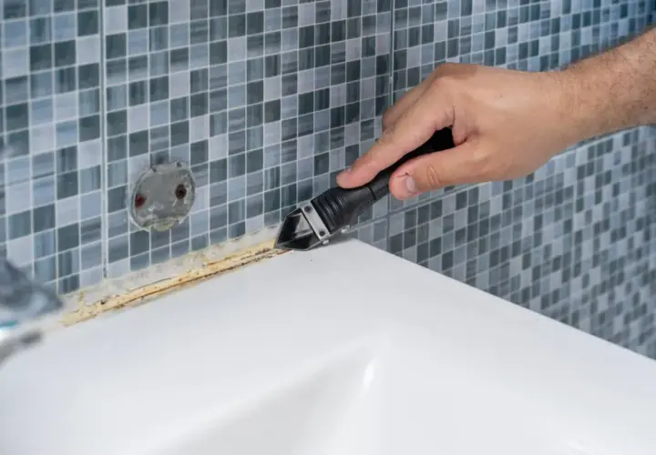 Mano usando herramienta para quitar silicona de plato ducha de resina.