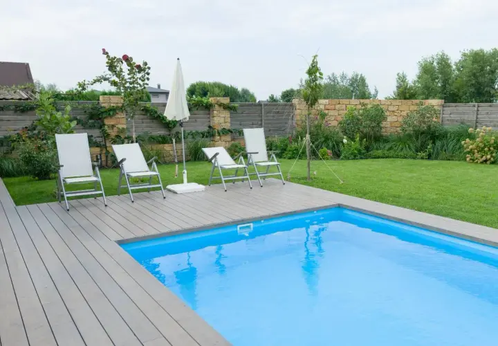 Sillas y sombrilla junto a la piscina, con un suelo de madera que rodea el agua azul.
