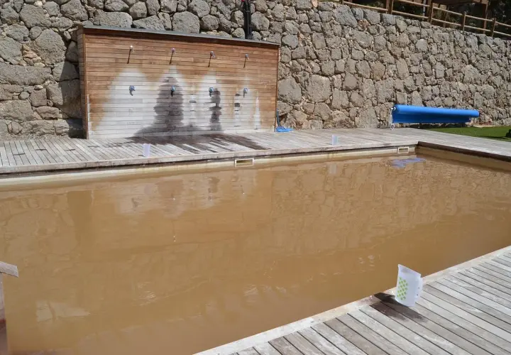 Una piscina de sal con agua turbia y una pared de duchas de madera.