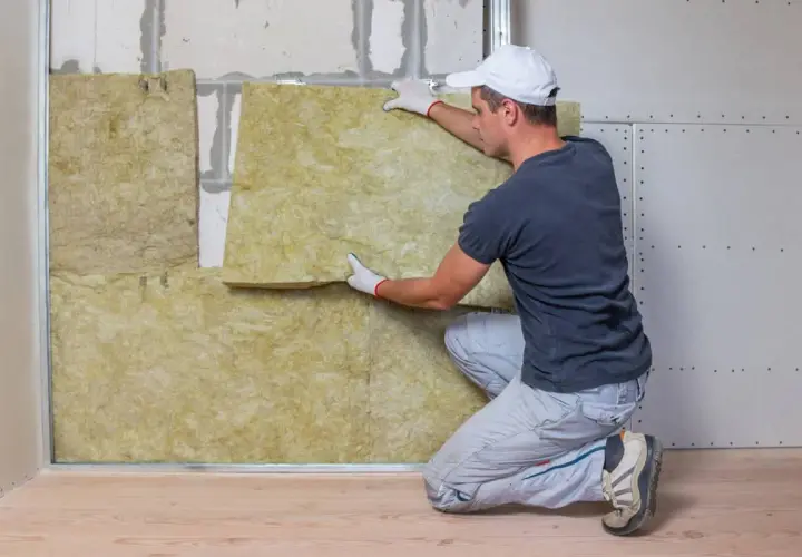 Obrero instala material aislante para aislar paredes del frío. La lana mineral se coloca entre perfiles metálicos.