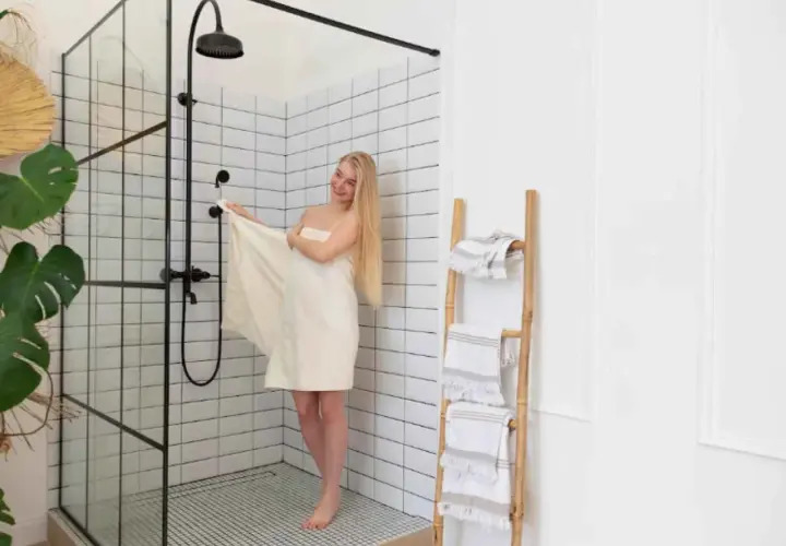 Mujer rubia envuelta en toalla junto a mampara de ducha moderna. Explora los tipos de mamparas de ducha para tu baño.