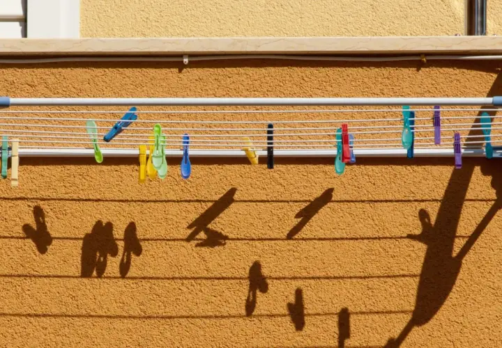 Variedad de pinzas de colores sujetan la ropa en distintos tipos de tendederos exteriores. Las sombras proyectadas crean un patrón interesante.