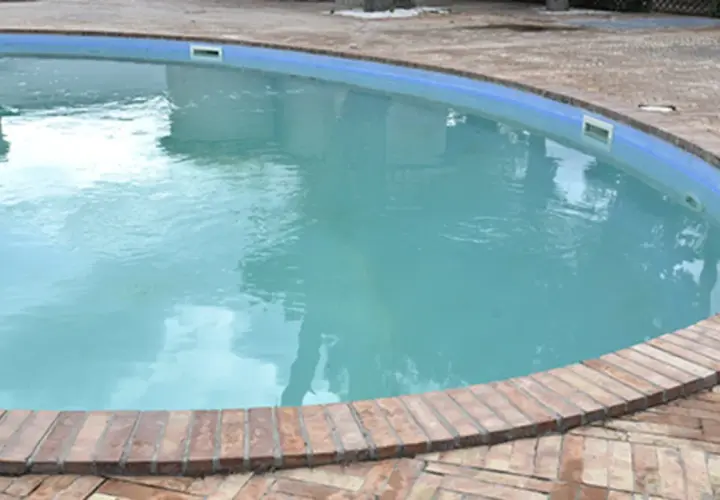 Agua blanca y cristalina en una piscina, rodeada por un borde de ladrillos. El reflejo del cielo en el agua invita a un refrescante chapuzón.