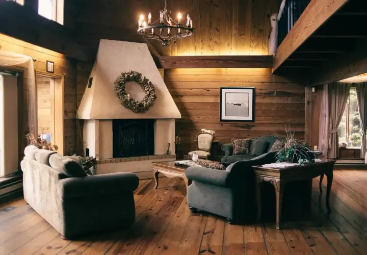 Salón rústico con chimenea de obra decorada con corona de hojas. Sofás cómodos y suelo de madera invitan a relajarse.
