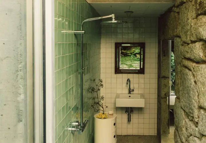 Baños pequeños con ducha, lavabo y espejo con vista a un jardín. Paredes de azulejos verdes y piedra natural.