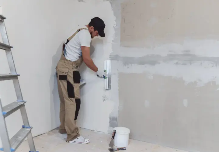 Un obrero aplica yeso a una pared con una llana. Aprende como hacer yeso para renovar tu hogar.