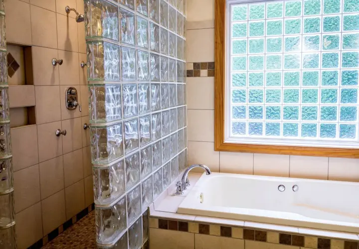Duchas con paves de vidrio separan la bañera de la zona de ducha. La luz se filtra a través de la ventana de paves.