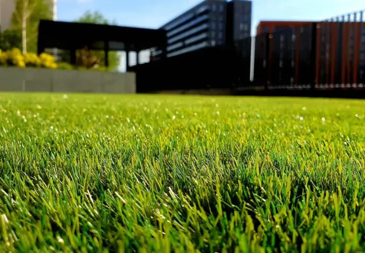 Césped artificial verde y vibrante, perfecto para aprender como limpiar cesped artificial y mantenerlo impecable. Edificios modernos al fondo.