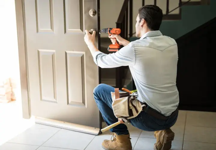 Hombre con taladro y cinturón de herramientas, aprendiendo como desmontar una cerradura de puerta interior.