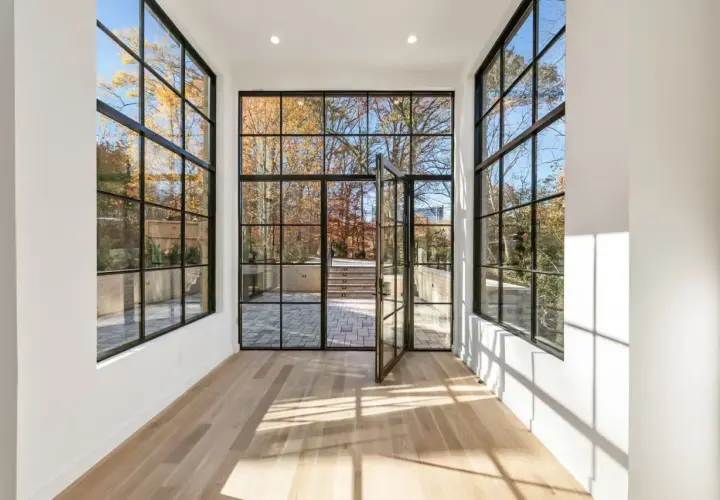 Amplio salón con grandes ventanales de aluminio y madera que dan a un jardín otoñal.