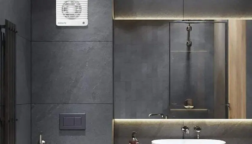 Extractor de baño blanco instalado en pared de azulejos grises.