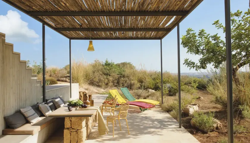 Porches sencillos y bonitos con mesa de piedra, asientos cómodos y tumbonas coloridas, disfrutando de vistas al campo.