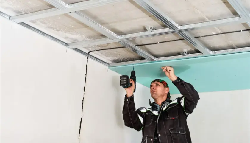 Un trabajador instala una placa de yeso verde en un techo metálico, un paso clave en como hacer una pared de pladur.