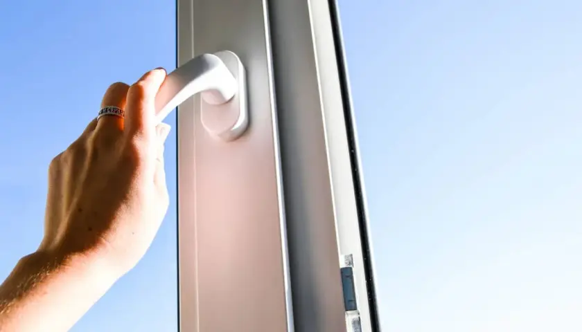 Mano girando la manija para reparar cierre ventana aluminio abatible. Cielo azul de fondo.