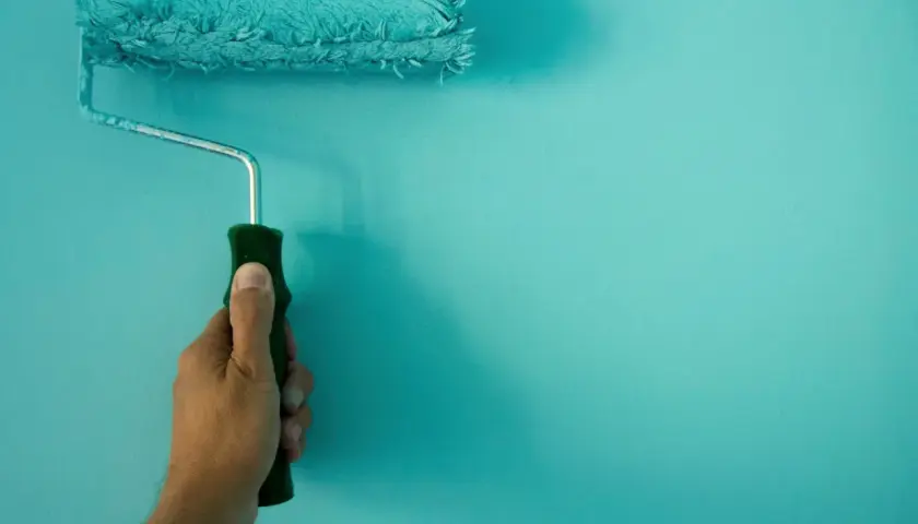 Mano sujetando un rodillo de pintura turquesa, ideal para conseguir el mejor rodillo para pintar paredes lisas.