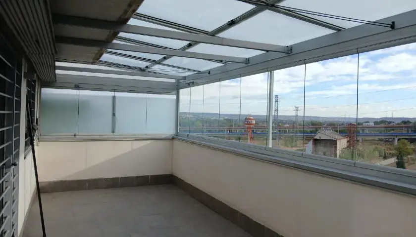 Terraza con cerramiento abatible de cristal, creando un espacio moderno y luminoso con vistas al exterior.