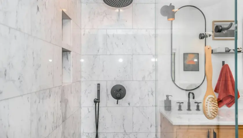Ducha empotrada con grifo negro y rociador superior. La pared de mármol blanco tiene nichos empotrados.