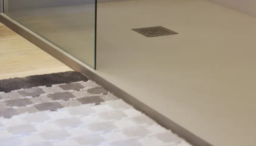 Plato de ducha blanco moderno con desagüe cuadrado. Alfombra a cuadros en primer plano.