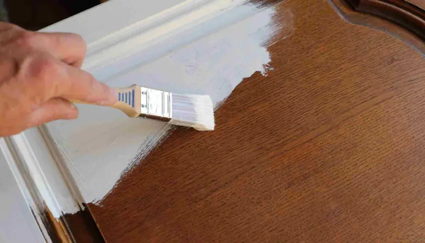 Pintando una puerta de madera ya pintada con brocha y pintura blanca.