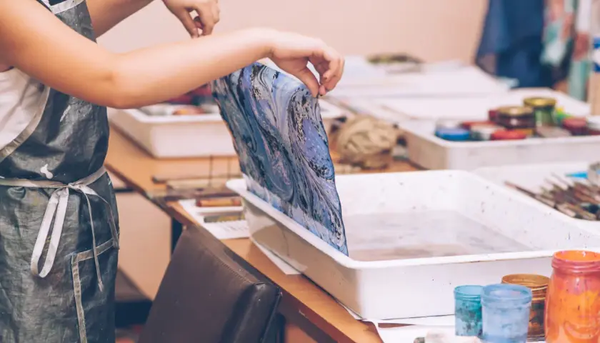 Manos sostienen tela con diseño marmoleado sobre una bandeja con agua, lista para la pintura para mármol.