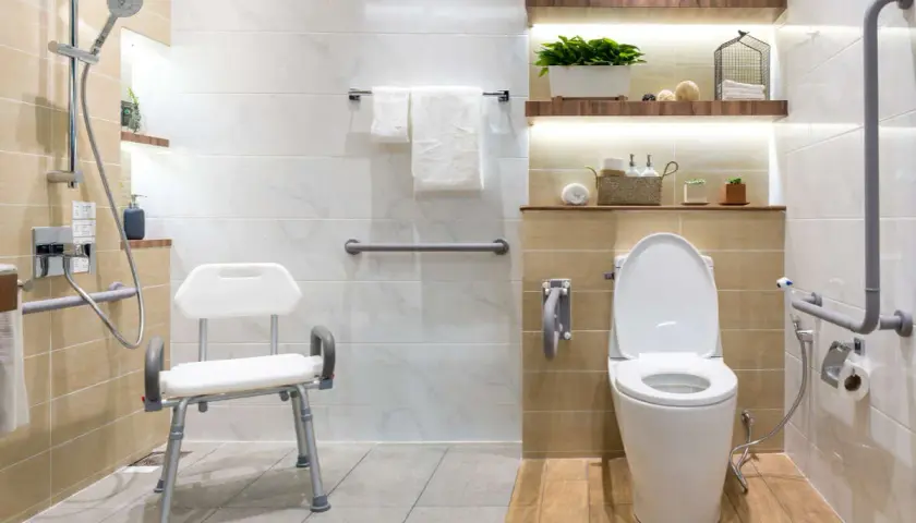 Baño moderno con duchas adaptadas para personas mayores, asiento de ducha, barras de apoyo y un inodoro.