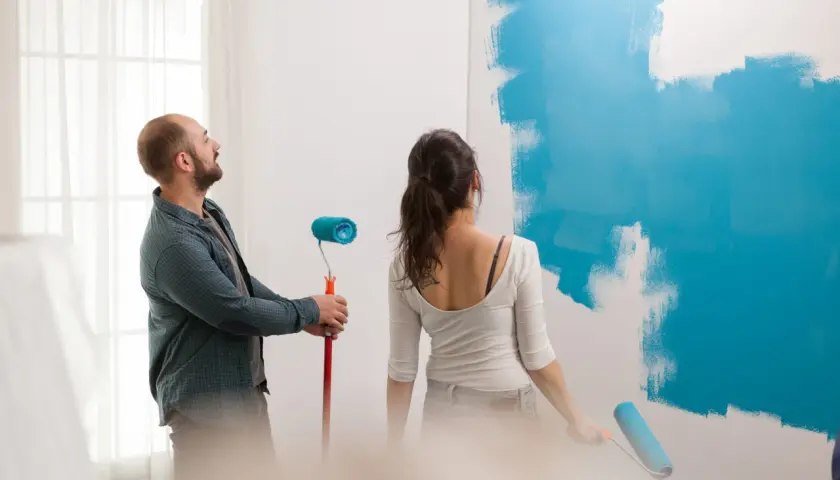 Pareja pintando una pared de azul. Él mira al techo, ella pinta. ¿Qué se pinta primero el techo o las paredes?
