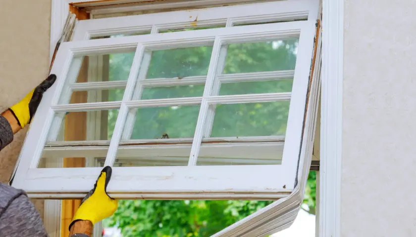 Manos enguantadas retiran un panel de ventana antiguo, imaginando cómo sería cuando se inventó el cristal para las ventanas.