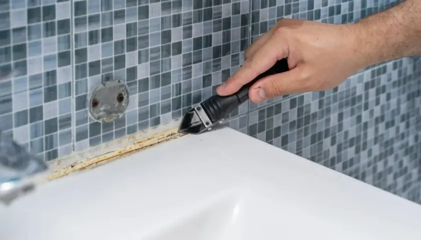 Mano usando herramienta para quitar silicona de plato ducha de resina.