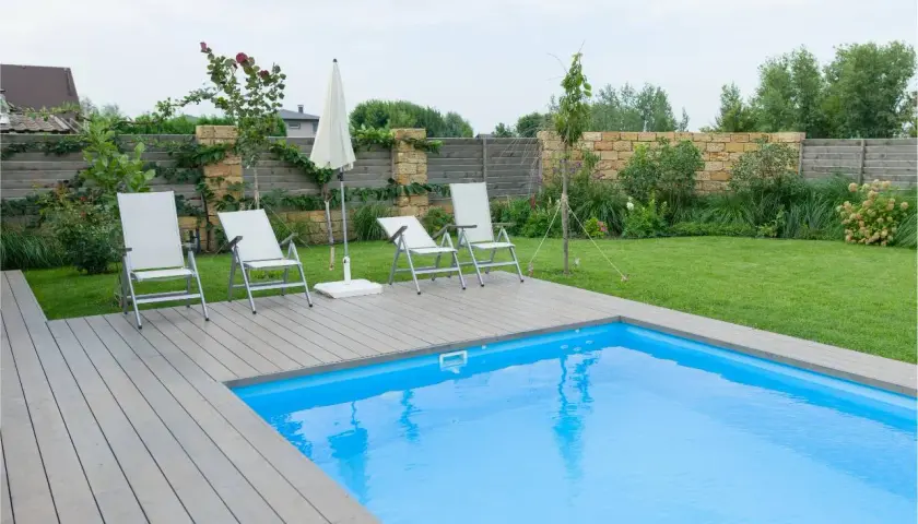 Sillas y sombrilla junto a la piscina, con un suelo de madera que rodea el agua azul.