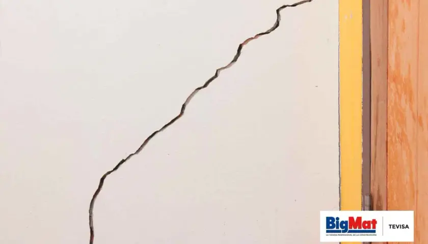 Grieta profunda en pared blanca, junto a marco amarillo y puerta de madera. Aprende como arreglar grietas profundas en paredes.