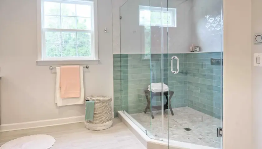 Instalar mampara ducha frontal corredera: baño moderno con ducha de cristal, azulejos verdes y ventana.