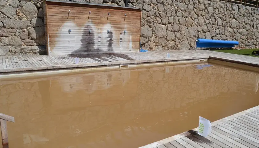 Una piscina de sal con agua turbia y una pared de duchas de madera.