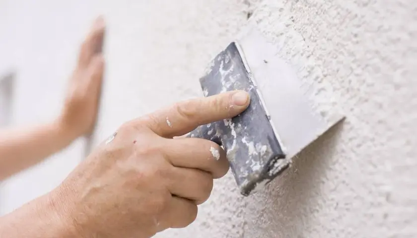 Mano aplicando masilla con espátula para reparar gotelé.