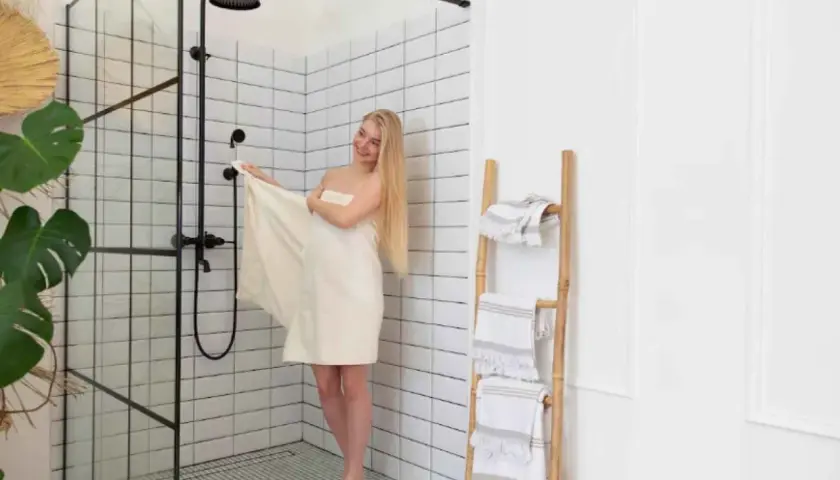 Mujer rubia envuelta en toalla junto a mampara de ducha moderna. Explora los tipos de mamparas de ducha para tu baño.