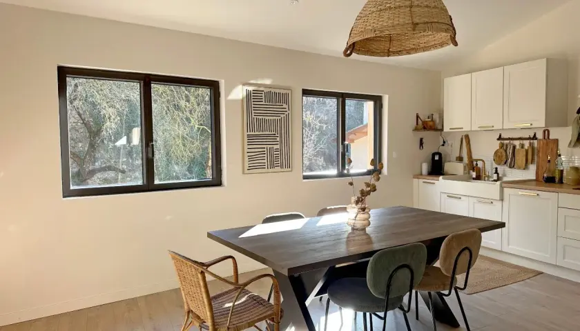 La cara de un cristal refleja la luz del sol en un comedor rústico con mesa de madera y sillas de mimbre.