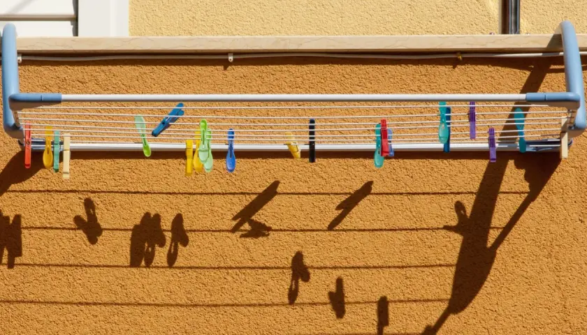 Variedad de pinzas de colores sujetan la ropa en distintos tipos de tendederos exteriores. Las sombras proyectadas crean un patrón interesante.
