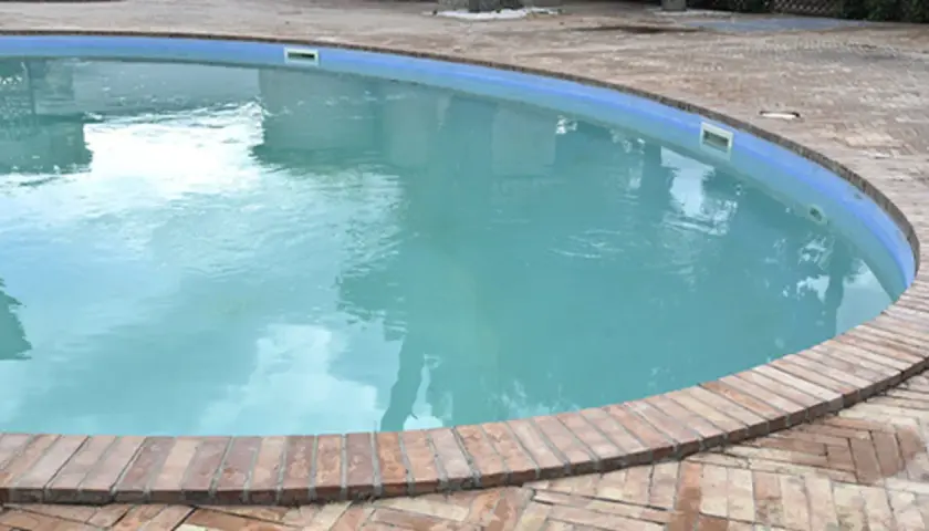 Agua blanca y cristalina en una piscina, rodeada por un borde de ladrillos. El reflejo del cielo en el agua invita a un refrescante chapuzón.