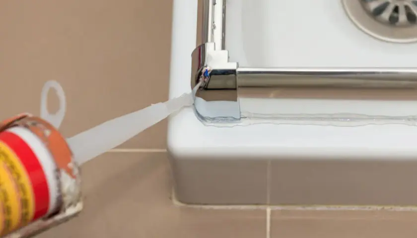 Aplicando sellador para mampara de ducha. Un aplicador de silicona deposita un cordón blanco para sellar la unión entre la mampara y la bañera.