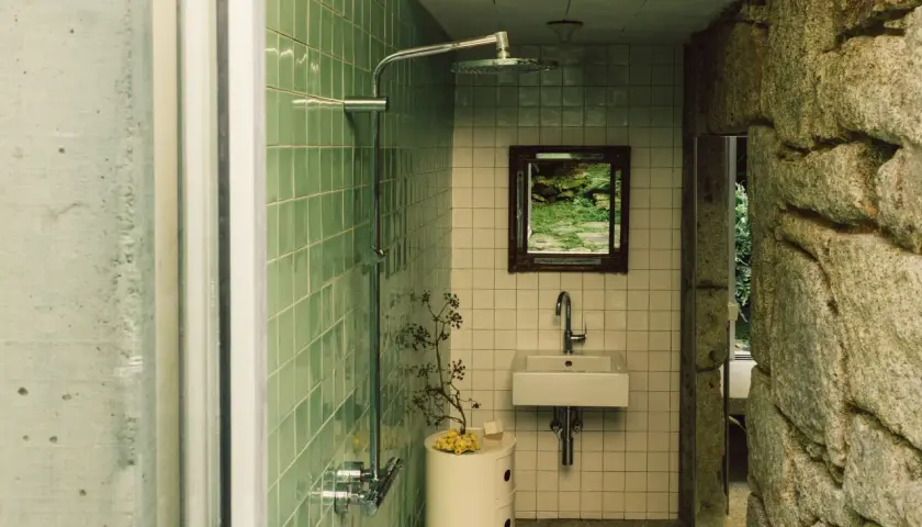 Baños pequeños con ducha, lavabo y espejo con vista a un jardín. Paredes de azulejos verdes y piedra natural.