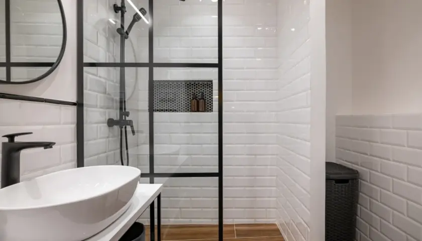 Modern bathroom with a glass-enclosed shower featuring white subway tiles and a built-in niche. The shower is adjacent to a wall, creating a functional space.