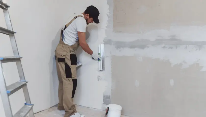 Un obrero aplica yeso a una pared con una llana. Aprende como hacer yeso para renovar tu hogar.