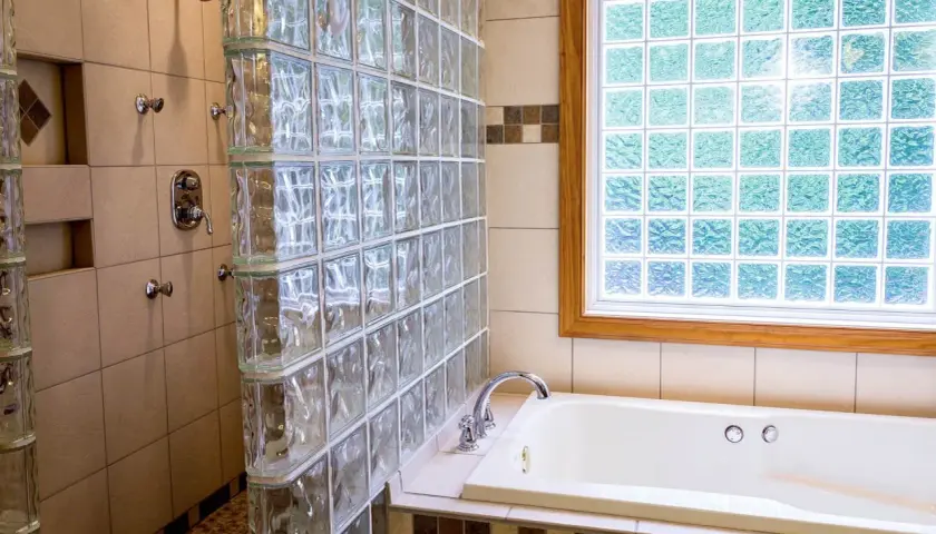 Duchas con paves de vidrio separan la bañera de la zona de ducha. La luz se filtra a través de la ventana de paves.