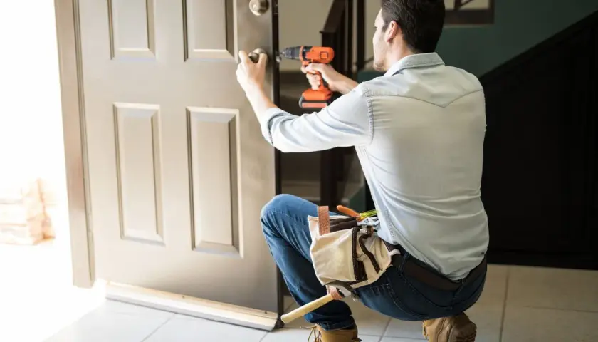 Hombre con taladro y cinturón de herramientas, aprendiendo como desmontar una cerradura de puerta interior.