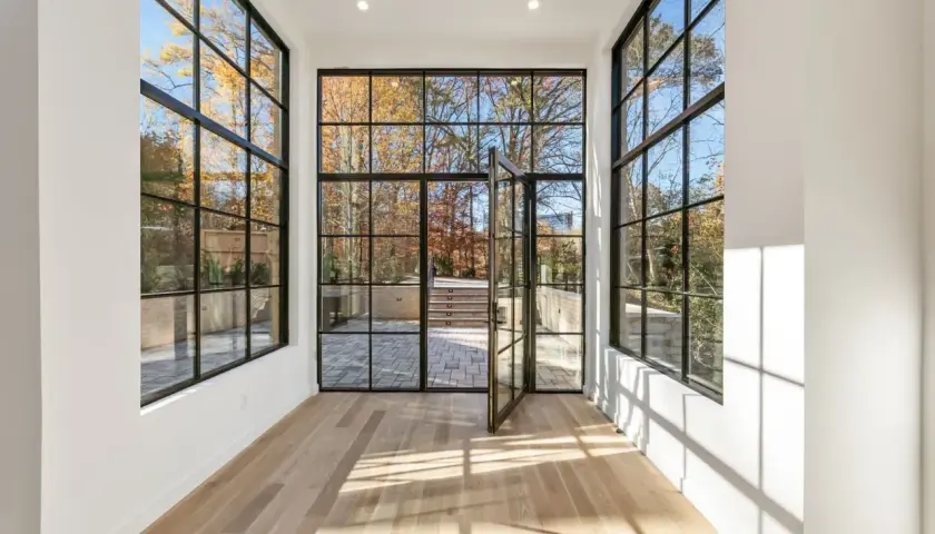 Amplio salón con grandes ventanales de aluminio y madera que dan a un jardín otoñal.