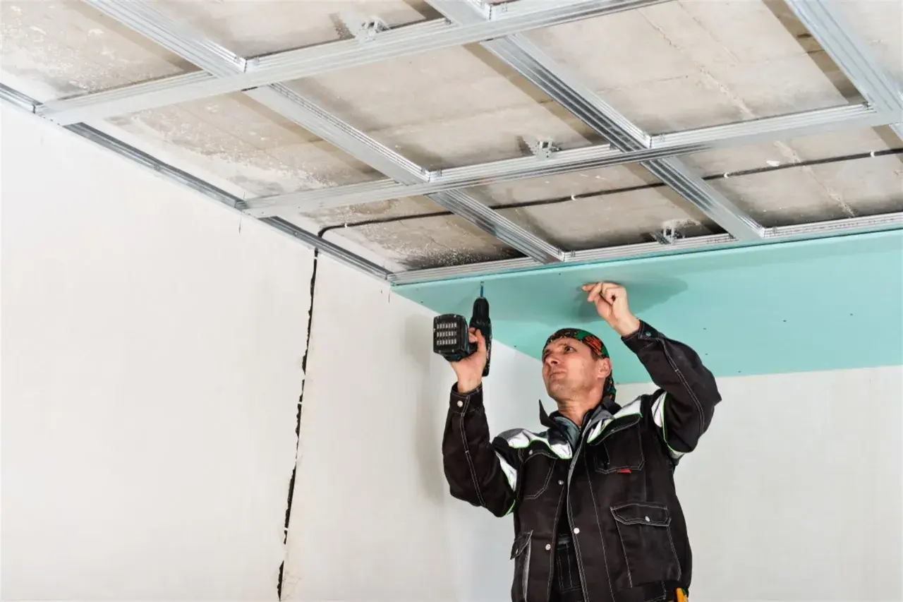 Un trabajador instala una placa de yeso verde en un techo metálico, un paso clave en como hacer una pared de pladur.