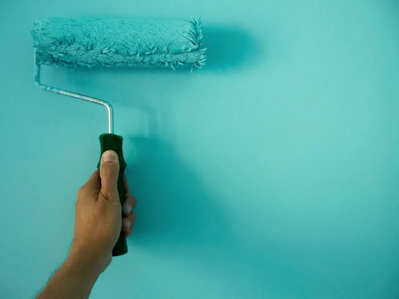 Mano sujetando un rodillo de pintura turquesa, ideal para conseguir el mejor rodillo para pintar paredes lisas.
