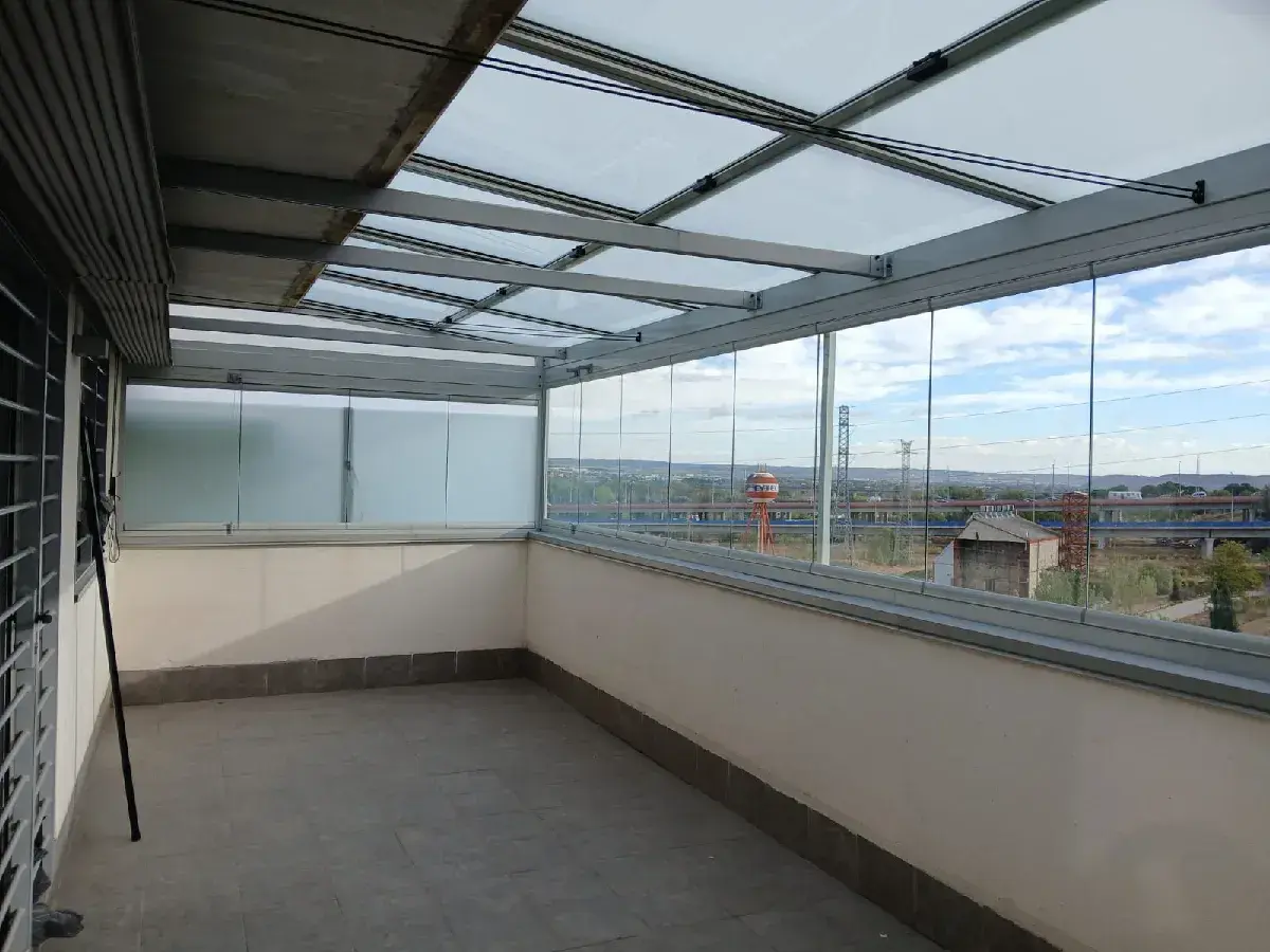 Terraza con cerramiento abatible de cristal, creando un espacio moderno y luminoso con vistas al exterior.